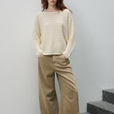 A woman stands on gray stone stairs against a light gray wall, wearing a cream ribbed knit sweater and wide-leg tan pants with white shoes.